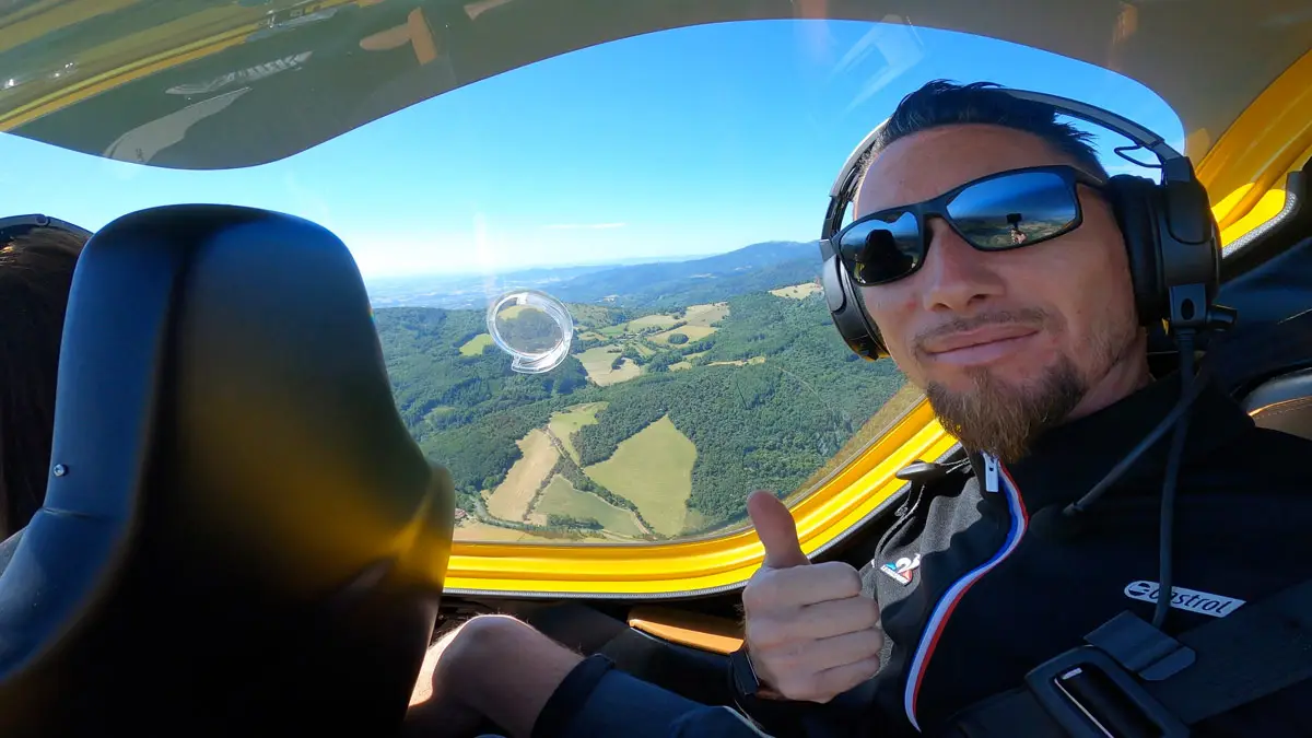 Passager casqué levant le pouce en vol au-dessus d'un paysage verdoyant